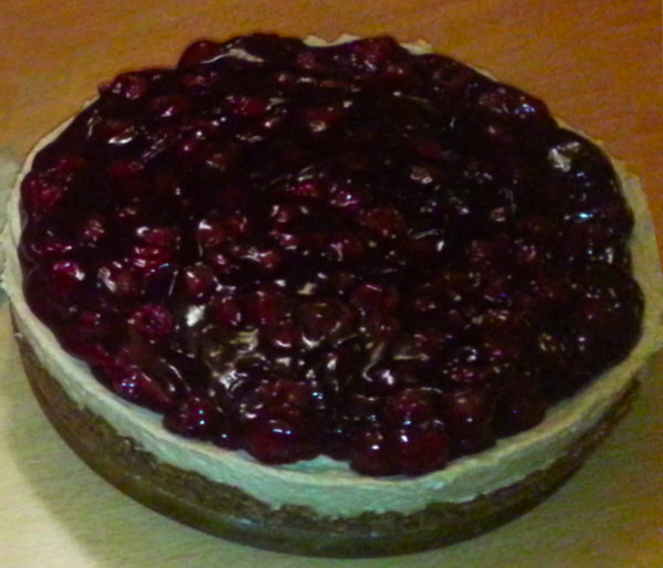 A round MonChou cake topped with a glossy layer of dark red cherries on a creamy filling and biscuit crust.