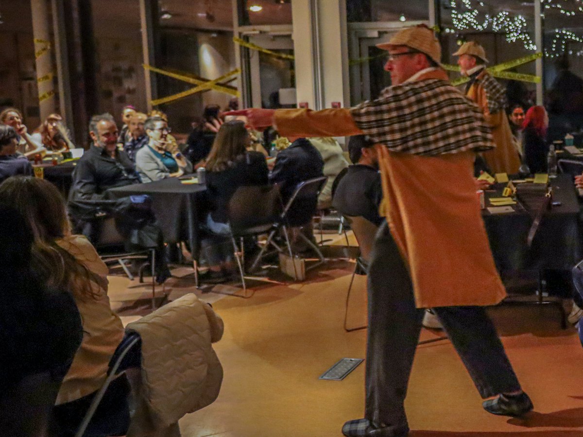 The detective striding between tables pointing at a suspect during Murder at the Museum, a Murder YOU Mystery at the Museum of Vancouver